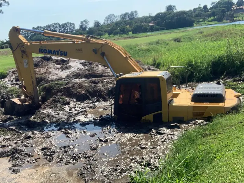 Escavadeira hidráulica Komatsu trabalhando em área encharcada, com lama até a altura da cabine