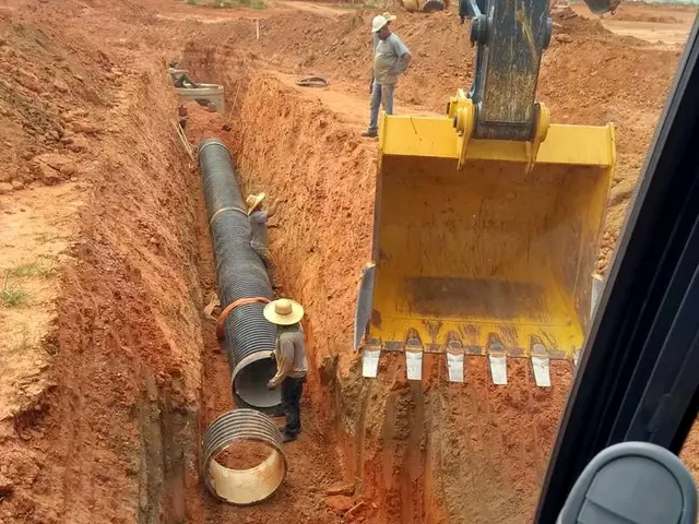 Instalação de tubo corrugado em vala funda, com a caçamba da escavadeira ao lado