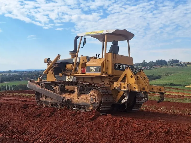 Trator de esteira Caterpillar D6 com lâmina e escarificador sobre terra vermelha